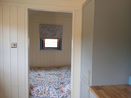 A narrow room with a window, a bed with floral bedding, and a wooden counter.