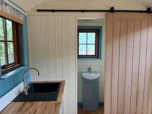 A bathroom with a wooden vanity, a sink, and a window with a view of greenery. - Woodie (Ludlow)