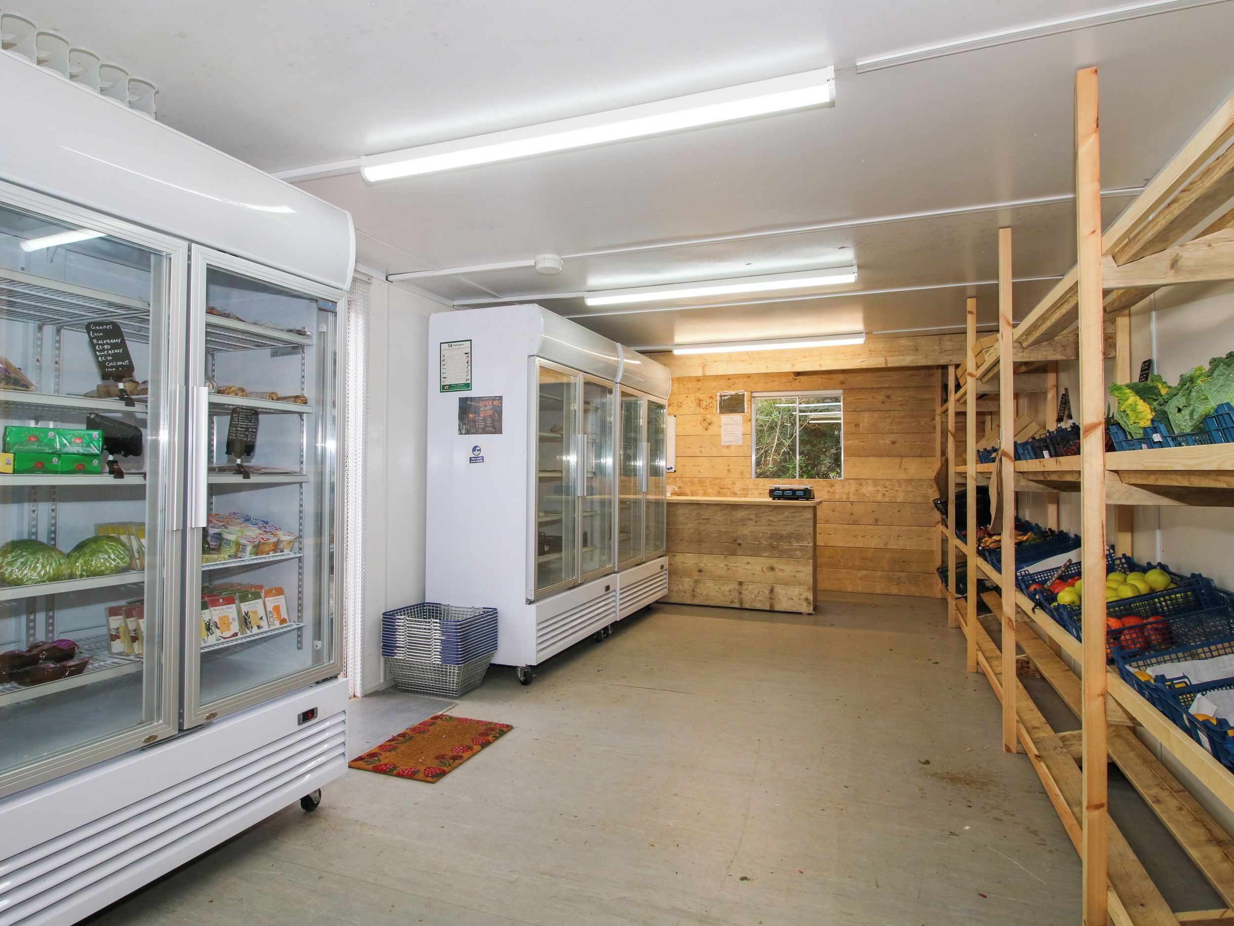 A grocery store interior with refrigerated display cases, wooden shelving, and a checkout counter.
