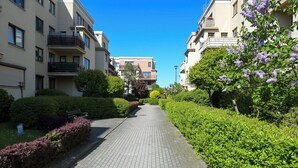 A paved pathway flanked by well-maintained hedges and trees, leading to a building with multiple balconies. - Apartament Agnes by Q4 Apartments  (Gdańsk)