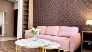 A modern living room with a pink sofa, a round table with a vase of flowers, and a patterned wall. - Apartament Agnes by Q4 Apartments  (Gdańsk)