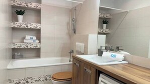A bathroom with a bathtub, toilet, sink, and shelves with plants. - Apartament Agnes by Q4 Apartments  (Gdańsk)