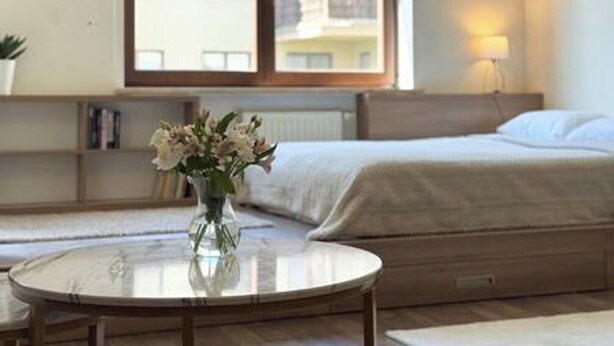 A bedroom with a bed, a bedside table with a vase of flowers, a window, and a lamp. - Apartament Agnes by Q4 Apartments  (Gdańsk)