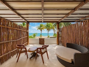 Un espace extérieur abrité, aménagé avec des sièges, et offrant une vue sur la plage et les palmiers.