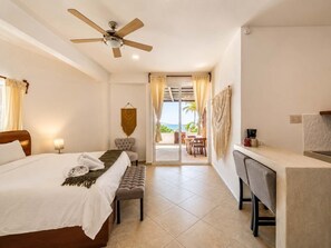 Ein Hotelzimmer mit Bett, Schreibtisch, Sessel und Deckenventilator, mit Blick ins Freie.