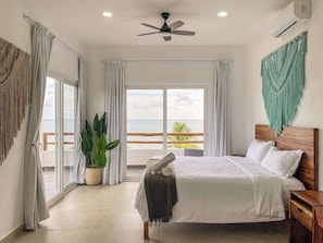 Une chambre avec un lit, un ventilateur de plafond, une plante en pot et une vue sur l’océan.