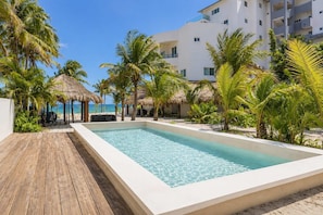 Une piscine dotée d’une terrasse en bois, entourée de palmiers et offrant une vue sur la plage.