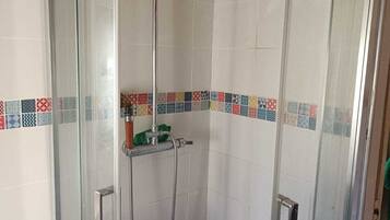 Une douche fermée par des parois en verre, dotée d’un pommeau de douche à main et d’un robinet fixé au mur.