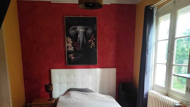 A bedroom with a large bed, a radiator, a window with curtains, and a painting on the wall. - 2-room apartment in a large, quiet house with garden and shared spaces (Vence)