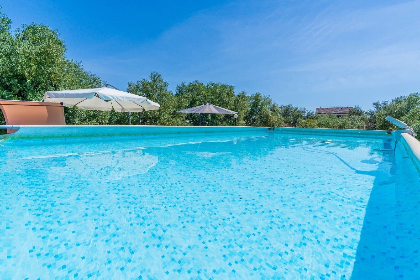 A clear blue pool with a tiled bottom, surrounded by trees and a clear sky.