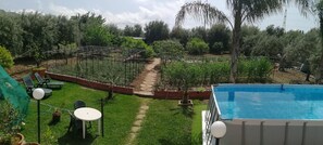 Un jardin avec une piscine, un potager avec différentes espèces de plantes et du mobilier d’extérieur.