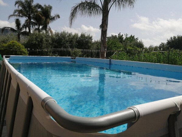 A clear blue swimming pool with a white poolside and a metal railing.