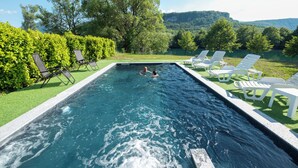 A rectangular swimming pool with clear water, surrounded by white lounge chairs and greenery.