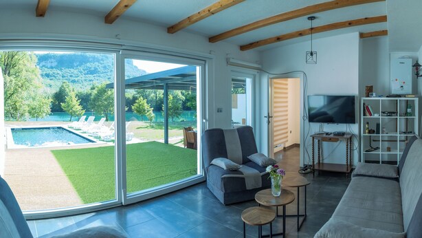 A modern living room with a sliding glass door leading to a pool, a sofa, a TV, and a small table with a vase.