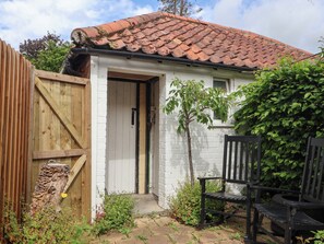 A small, single-story building with a tiled roof, a wooden gate, and a bench. - The Cooks Cottage (Malton)