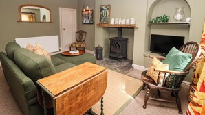 Een woonkamer met een groene bank, een houten salontafel, een televisie, een open haard en een decoratieve fauteuil.