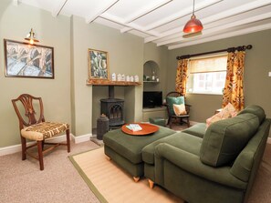 A cozy living room with a green sofa, a wooden chair, a fireplace, and a television. - The Cooks Cottage (Malton)