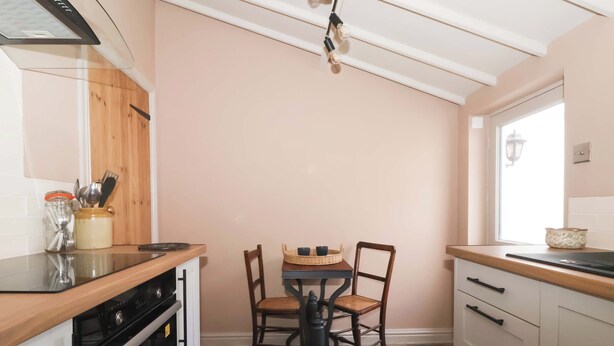 Een keuken met een houten aanrecht, een fornuis, een eettafel met stoelen en een raam.