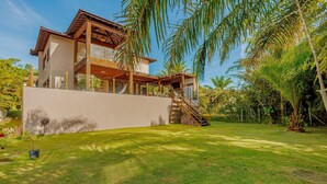 Ein modernes, zweistöckiges Haus mit Balkon, umgeben von üppiger Vegetation und einem gepflegten Rasen.