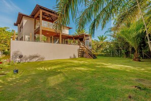 Ein modernes, zweistöckiges Haus mit Balkon, umgeben von üppiger Vegetation und einem gepflegten Rasen.