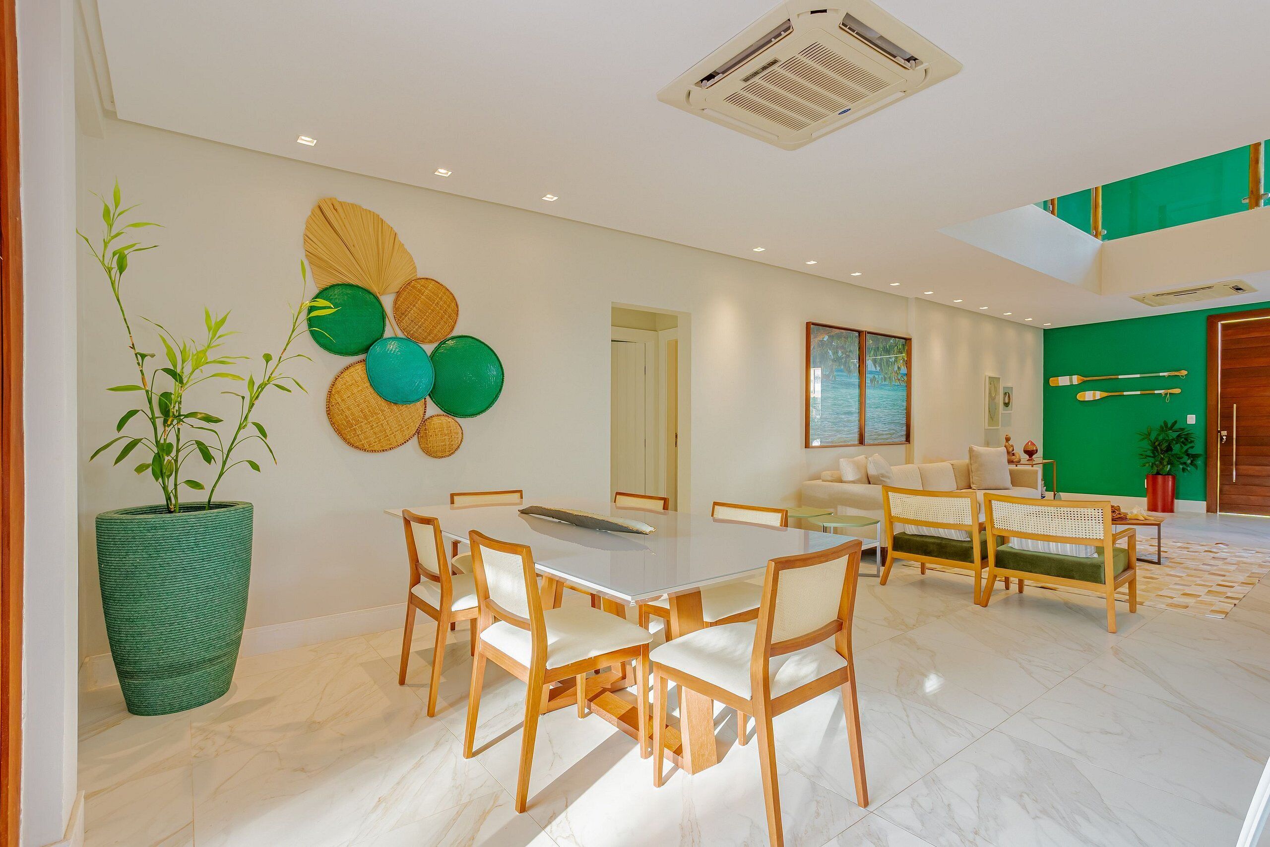 A modern interior with a dining area, sofas, a large potted plant, and a green accent wall.