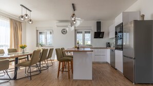 A modern kitchen with a central island, stainless steel appliances, and a dining area with a table and chairs. - Apartment Temida with sea view (Rovanjska)