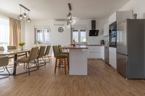 A modern kitchen with a central island, stainless steel appliances, and a dining area with a table and chairs. - Apartment Temida with sea view (Rovanjska)