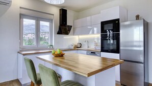 A modern kitchen with a central island, stainless steel appliances, and a view through a window. - Apartment Temida with sea view (Rovanjska)