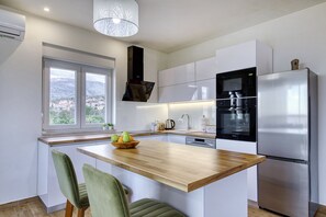 A modern kitchen with a central island, stainless steel appliances, and a view through a window. - Apartment Temida with sea view (Rovanjska)