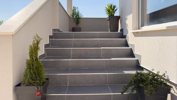 A set of exterior stairs leading to a building entrance, with potted plants and a clear sky. - Apartment Temida with sea view (Rovanjska)