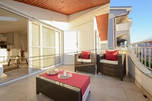 Ein Balkon mit Korbmöbeln, eine Glastür, die zu einem Raum führt, und eine rote Tischdecke.