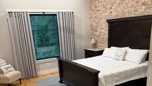 A bedroom with a large window, a bed with a dark headboard, a nightstand, a chair, and a ceiling fan. - Stunning gated ranch w/ breathtaking views and modern amenities, on 103 acres. (Sand Springs)