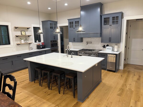 A modern kitchen with grey cabinets, a central island with stools, a stove, and overhead pendant lights.