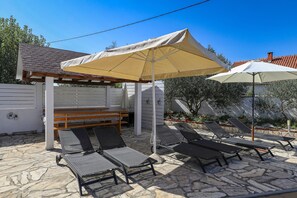 Eine Terrasse mit Steinboden, Sitzgelegenheiten im Freien und Sonnenschirmen, die Schatten spenden.