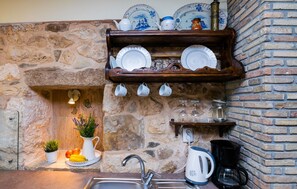 Eine Küche mit Steinwand, einem Holzbodenregal mit Geschirr, einer Spüle und einer Kaffeemaschine.