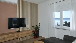Una sala moderna con un televisor de pantalla plana, una mesa consola de madera, una planta en maceta, un sofá y una ventana con vistas.