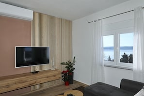 Ein modernes Wohnzimmer mit Flachbildfernseher, einem Holztischchen, einer Topfpflanze, einer Couch und einem Fenster mit Blick.
