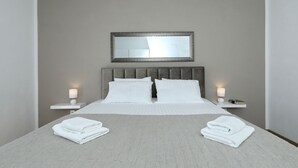Una habitación de hotel con una cama, dos mesitas de noche, un tocador, un espejo y toallas dobladas sobre la cama.