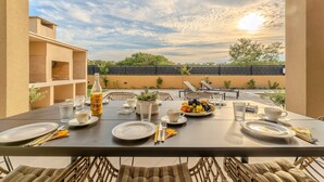 A dining table set with plates, cutlery, and a fruit bowl, overlooking a building and trees under a clear sky. - Holiday Home Pecora Nera with Pool (Ražanac)
