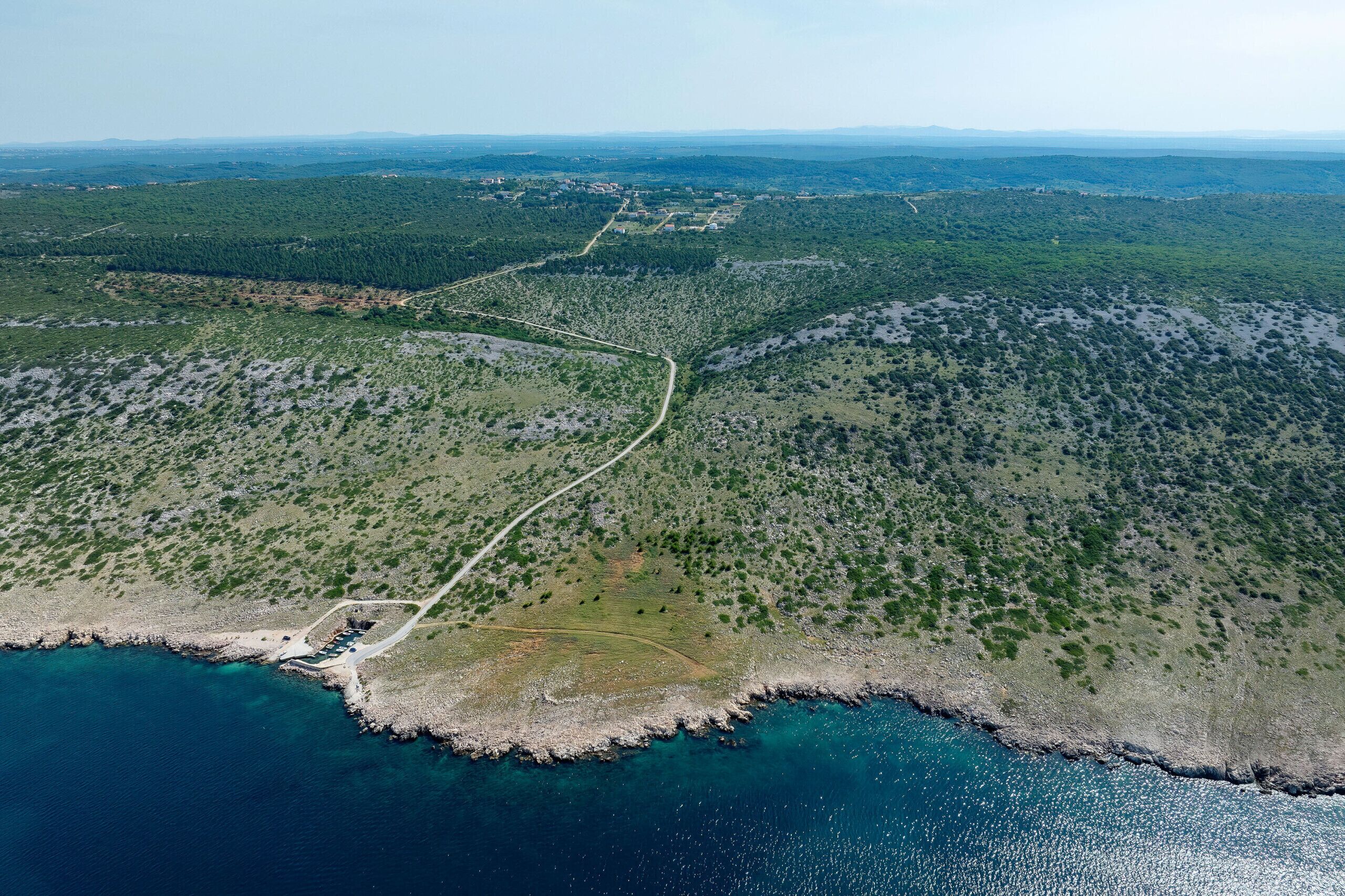 Luftaufnahme einer Küstenregion mit einer Straße, die zu einem Gebäudekomplex in Strandnähe führt.
