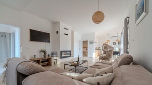 A modern living room with a large beige sofa, a coffee table, and a television. There is a wicker chair and a dining area in the background. - Holiday Home Pecora Nera with Pool (Ražanac)