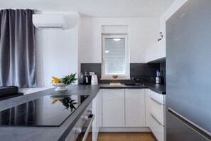 Eine moderne Küche mit schwarzer Arbeitsplatte, weißen Schränken, einem Einbauofen und einem Fenster mit Jalousien.