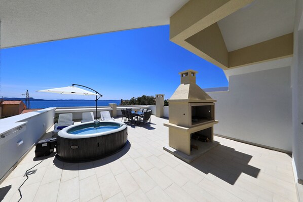Eine Dachterrasse mit Whirlpool, Sitzgelegenheiten im Freien und einem Grill.