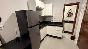 A compact kitchen with white cabinets, a black refrigerator, a microwave, and a sink. - Loft127-01 Compact, equipped, great location (Itajaí)