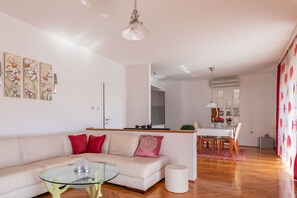 Ein Wohnzimmer mit einer Couch, einem Glastisch und einem Essbereich mit Tisch und Stühlen.