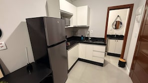 Eine kleine Küche mit weißen Schränken, einem schwarzen Kühlschrank, einer Mikrowelle und einem Spülbecken.