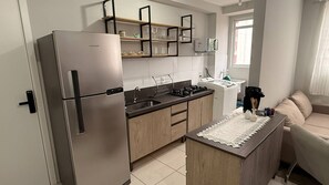 Eine kleine Küche mit Edelstahlkühlschrank, Holzschränken, einem Spülbecken und einer kleinen Kochinsel mit Spitzenleinentischdecke.