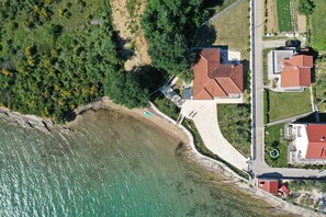 Eine Luftaufnahme einer Küstenimmobilie mit Strand, gepflastertem Weg und einem Gebäude mit rotem Dach.