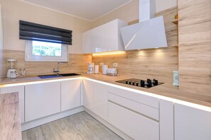Eine moderne Küche mit weißen Schränken, einem eingebauten Herd, einem Fenster mit Jalousien und einer Holzrückwand.