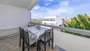 A balcony with a table and chairs, a white railing, and a view of buildings and greenery. - Apartment Perinic No.1 in Vrsi (Vrsi)